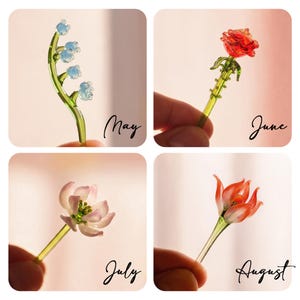 May include: Four glass flower figurines labeled May, June, July, and August. May features blue lily-of-the-valley on a green stem. June is a red rose with a green stem. July is a pink and white flower. August is an orange and white flower.