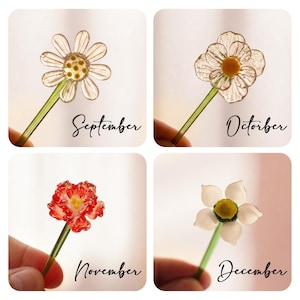 May include: Four glass flower stirrers with green stems. The September stirrer has a clear daisy, October has a clear flower with a yellow center, November has a red ruffled flower, and December has a white flower with a yellow center.