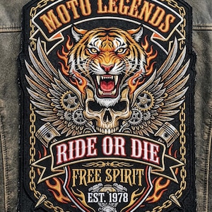 Può includere: Una grande toppa ricamata su una giacca in pelle marrone invecchiata con una testa di tigre ruggente sopra un teschio, fiancheggiata da ali, ingranaggi e pistoni. Il testo recita MOTO LEGENDS, RIDE OR DIE, FREE SPIRIT e EST. 1978 in arancione e bianco.