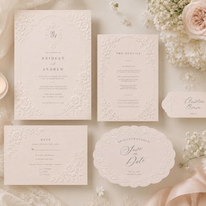 Könnte beinhalten: Ein Set aus blassrosa Hochzeitspapeterie mit geprägten Blumenrändern. Die Kollektion umfasst eine rechteckige Einladung, eine Detailkarte, eine Antwortkarte, eine gewellte, ovale Save-the-Date-Karte und ein kleines Namensschild mit eleganter Serifenschrift.
