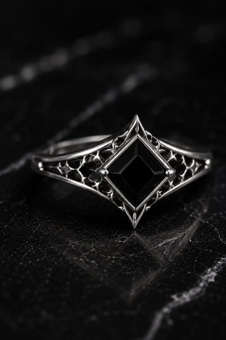 May include: A silver ring featuring a square-cut black gemstone set in a diamond-shaped frame. The band displays an intricate, openwork lattice design that extends from the central setting, showcasing a polished metallic finish throughout.