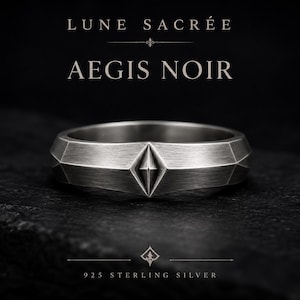 Pode incluir: Um anel de prata escovada com um relevo geométrico central em forma de diamante. O texto LUNE SACRÉE e AEGIS NOIR aparece acima do anel, enquanto 925 STERLING SILVER está impresso abaixo, acompanhado por um pequeno emblema decorativo.