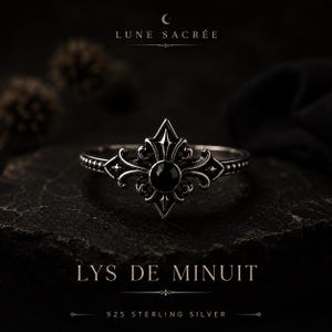 May include: A 925 sterling silver ring featuring a central black stone set within an ornate fleur-de-lis design. The band has a beaded texture. Text on the image reads LUNE SACREE, LYS DE MINUIT, and 925 STERLING SILVER.