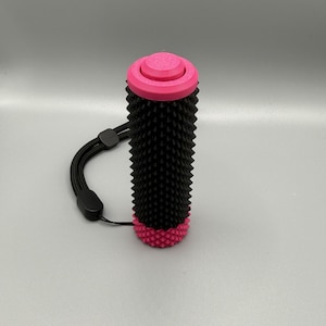 May include: A black and pink textured grip with a wrist strap. The grip has a cylindrical shape with a pink top and bottom. The main body is black with a spiky texture. A black wrist strap is attached to the grip.