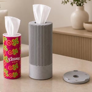 Może przedstawiać: Cylindryczny różowy pojemnik na chusteczki Kleenex on the go we wzór czerwonych grejpfrutów i zielonych liści, obok wyższego, żebrowanego szarego cylindrycznego dozownika na chusteczki z pasującą szarą okrągłą pokrywką leżącą obok.