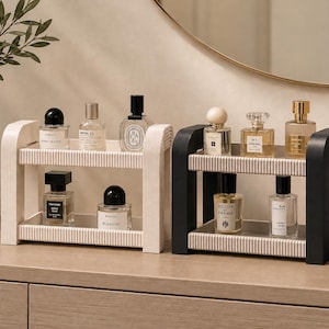 Pode incluir: Duas prateleiras de armazenamento retangulares de dois níveis, uma branca e outra preta, com suportes laterais canelados e bandejas planas. Cada prateleira contém vários frascos de perfume de vidro com tampas e rótulos distintos.
