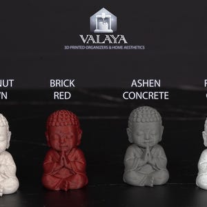May include: A product image displays four small Buddha statues in different colors: chestnut brown, brick red, ashen concrete, and forest green. The statues are arranged in a row, with the text "VALAYA 3D PRINTED ORGANIZERS & HOME AESTHETICS" at the top.