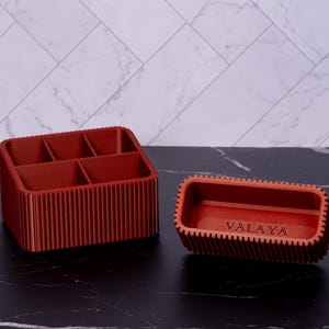May include: Two terracotta-colored organizers. One is rectangular with six compartments, the other is a smaller rectangular tray. The word "VALAYA" is etched on the smaller tray. Both have a ribbed design.