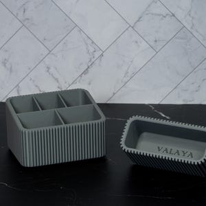 May include: Two gray organizers with vertical ribbed sides. One is a rectangular box with five compartments. The other is a smaller rectangular tray with the word "VALAYA" printed on the bottom.