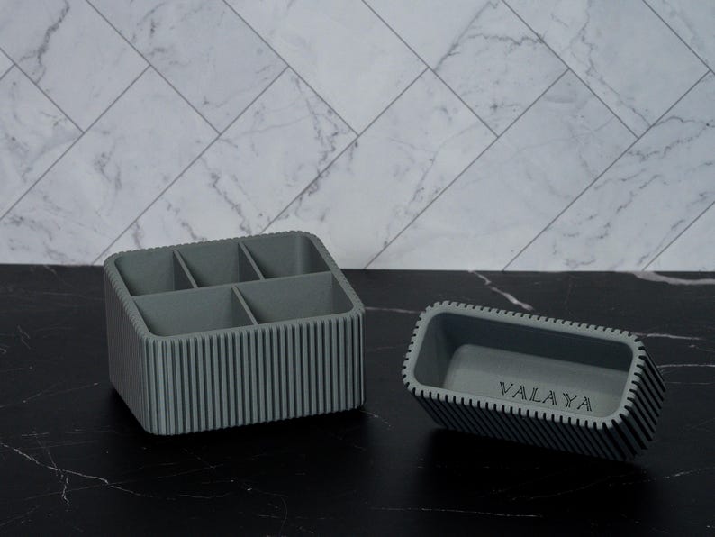 May include: Two gray organizers with vertical ribbed sides. One is a rectangular box with five compartments. The other is a smaller rectangular tray with the word "VALAYA" printed on the bottom.