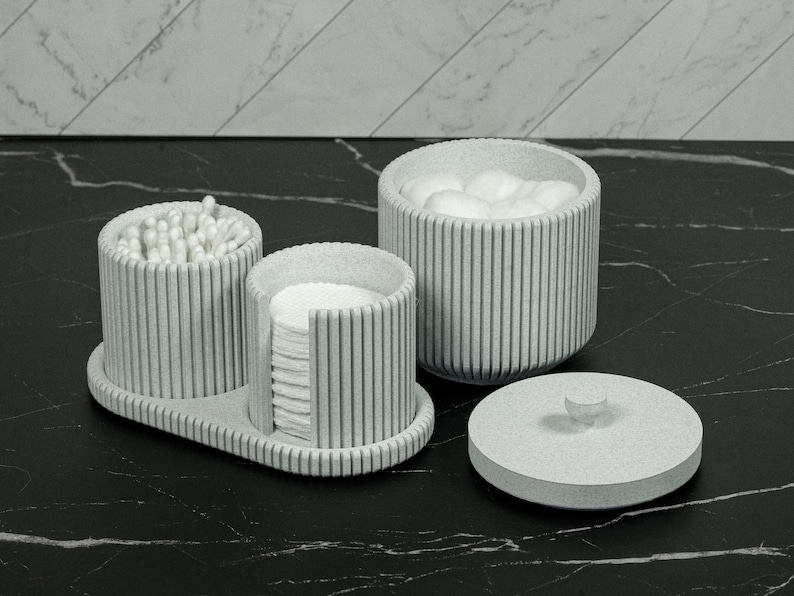 May include: A set of three light gray bathroom organizers. One container holds cotton balls, another holds cotton swabs, and a third holds cotton pads. A matching lid sits nearby. The organizers have a vertical striped design.