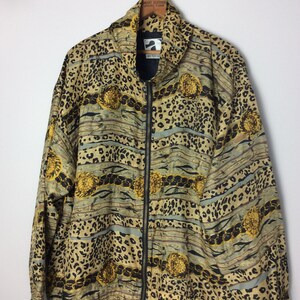 Puede incluir: Una chaqueta con estampado dorado, negro y marrón con cierre de cremallera. La chaqueta tiene un diseño de estampado de leopardo con un patrón de cadena.