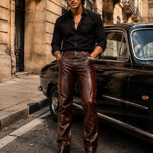 Pode incluir: Uma camisa preta de manga comprida com botões e colarinho, combinada com calças de couro castanho escuro de corte reto, com fecho de botões e presilhas para cinto. O visual é completado com sapatos sociais de couro preto e um colar.