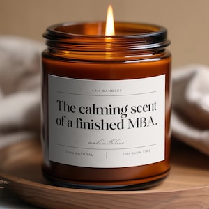 Puede incluir: Una vela encendida en un frasco de vidrio ámbar con una etiqueta blanca que presenta el texto 4AM CANDLES, The calming scent of a finished MBA., made with love, 100% NATURAL y 50H BURN TIME. La vela tiene una llama visible en un frasco cilíndrico.