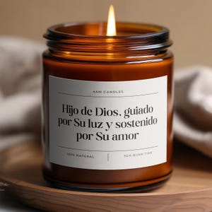 May include: A lit candle in a brown glass jar with a white label. The label reads "4AM CANDLES" and a Spanish phrase. The candle is on a wooden tray. The candle is labeled "100% NATURAL" and has a 50-hour burn time.