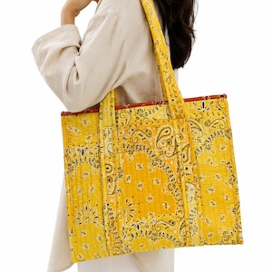 Può includere: Una borsa tote trapuntata rettangolare caratterizzata da una vivace stampa bandana gialla con motivi paisley neri. La borsa presenta due lunghi spallacci e una fodera interna rossa a contrasto visibile lungo il bordo superiore.
