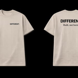 May include: A beige t-shirt with the word "DIFFERENT" printed in black on the front and back. The back of the shirt also has the text "Built, not born." The shirt has a crew neck and short sleeves.