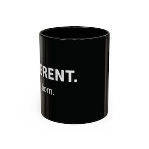 May include: A black ceramic mug featuring white text that reads "ERENT." on the top line and "not born." on the bottom line. The mug has a cylindrical shape with a smooth, glossy finish and a simple, clean design for daily beverage use.