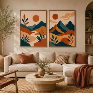 Puede incluir: Dos láminas de arte mural rectangulares con ilustraciones de paisajes abstractos que incluyen montañas, soles y follaje en tonos terracota, azul oscuro y crema. Las obras están expuestas en marcos de madera fina y simétrica.