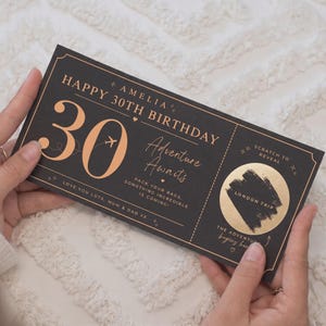 May include: A black rectangular birthday gift ticket with rose gold text and graphics. It reads: AMELIA HAPPY 30TH BIRTHDAY, Adventure Awaits, PACK YOUR BAGS, SOMETHING INCREDIBLE IS COMING!, LOVE YOU LOTS, MUM & DAD XX, and a scratch-off circle labelled LONDON TRIP.