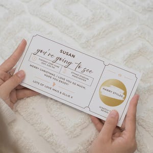 May include: A white rectangular event ticket with black text reading Susan, you're going to see, Tuesday 22nd June 2027, 5:00 PM, Etihad Stadium Manchester, Merry Christmas, I love you so much, hope you enjoy, lots of love Mais & Ollie X, and a gold scratch-off circle with Harry Styles text.