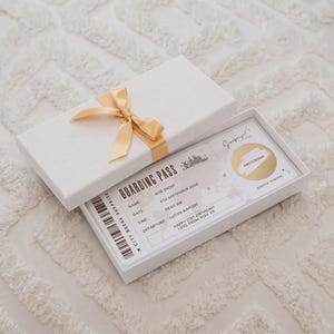 Puede incluir: Una caja de regalo rectangular blanca con una cinta dorada que contiene una tarjeta de embarque con el texto City Break Surprise, Boarding Pass, Rob Snow, 4th September 2026, 08:00 AM, Luton Airport, Happy 21st Birthday! Love from Alex XX, y Amsterdam.