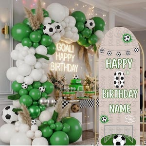 Puede incluir: Una decoración de cumpleaños con un gran arco de globos verdes y blancos con detalles de balones de fútbol. Un letrero arqueado muestra el texto HAPPY 0TH BIRTHDAY NAME con un gráfico de balón, un número cero y una portería de fútbol.