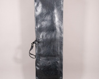 Puede incluir: Una funda larga negra, similar al cuero, con una correa para el hombro y un bolsillo. La funda tiene una superficie texturizada y una forma rectangular, diseñada para guardar un objeto largo y delgado. El bolsillo tiene un cierre de solapa.