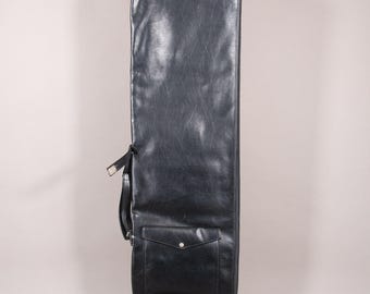Puede incluir: Un estuche de guitarra de cuero negro con forma rectangular. El estuche tiene un asa, un bolsillo con cierre de botón y un ribete rojo en la parte inferior. El estuche está diseñado para proteger una guitarra.