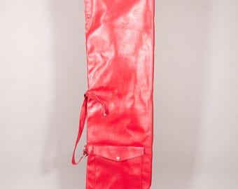 Puede incluir: Una bolsa larga roja para palos de golf, de material similar al cuero, con un bolsillo y cierre de cordón. Diseñada para guardar palos de golf, tiene una correa para el hombro. La bolsa es de color rojo vibrante y de material duradero.