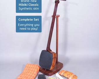 Puede incluir: Un shamisen Hibiki Classic, un instrumento tradicional japonés de tres cuerdas, hecho de madera oscura, con una piel sintética. La imagen incluye un juego completo con accesorios y el texto "Brand-new Hibiki Classic Synthetic skin" y "Complete Set Everything you need to play!"