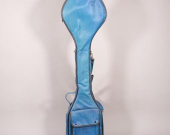 Puede incluir: Una funda de banjo azul claro con ribete gris. La funda tiene un cuerpo largo y delgado con una parte superior redondeada y un bolsillo rectangular en la parte inferior. Cuenta con un asa y una correa para el hombro.