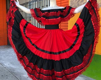 Può includere: Un abito lungo fino ai piedi con spalle scoperte in un vivace schema di colori rosso e nero. Il capo presenta un ampio scollo a volant, una vita aderente e una gonna voluminosa decorata con fasce nere orizzontali e pizzo rosso intricato.