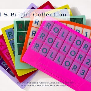 Op de afbeelding: Een verzameling kleurrijke Mah Jongg kaarthouders in verschillende kleuren, waaronder roze, rood, groen en geel. Elke houder heeft een raster met het woord "ROLLOR" en cijfers. De tekst "Bold & Bright Collection" is zichtbaar.