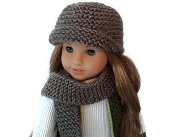 May include: A doll wearing a gray knitted hat and scarf. The doll has long brown hair and green eyes.
