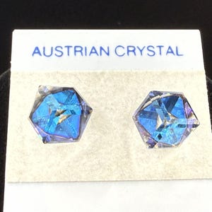 May include: A pair of hexagonal blue crystal stud earrings. The earrings are displayed on a white card with the text "AUSTRIAN CRYSTAL" in blue. The crystals have a multifaceted design, reflecting light.