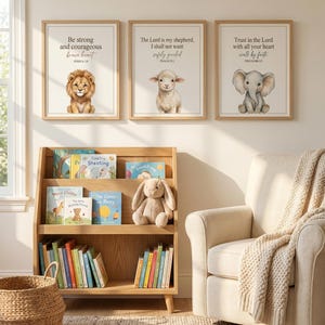 May include: Three framed wall prints featuring a lion, a lamb, and an elephant with religious text. Below, a light wood bookshelf holds children's books and a plush rabbit toy. A cream-colored armchair with a textured throw blanket sits nearby.