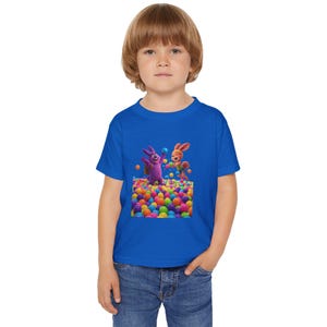May include: A royal blue toddler t-shirt featuring a colorful graphic of two cartoon bunnies playing in a ball pit filled with multi-colored balls. The bunnies are purple and orange. The shirt is made of soft material.