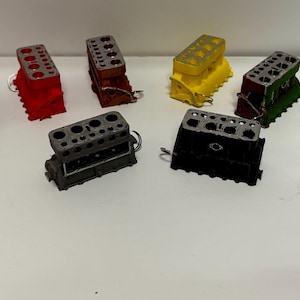 May include: A collection of miniature engine block models in various colors, including orange, black, red, brown, yellow, green, gray, white, and blue. Each model has a detailed design with multiple holes and a small metal ring attached.