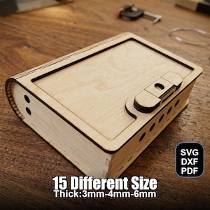Può includere: Una scatola di legno color chiaro con forma rettangolare e dorso curvo, con chiusura a scatto. La scatola presenta una serie di piccoli fori sul lato e il testo "15 Different Size Thick:3mm-4mm-6mm".