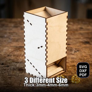 May include: A wooden dice tower with a rectangular design. The tower is made of light-colored wood with a contrasting white side featuring decorative cutouts. The text "3 Different Size Thick: 3mm-4mm-6mm" is visible. Two yellow dice are at the base.