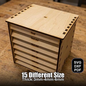 Könnte beinhalten: Eine hellfarbene Holzkiste mit mehreren horizontalen Schlitzen, beschriftet mit Text wie "Tool" und "Test out". Die Kiste hat eine quadratische Form mit einem Deckel und ist mit "15 Different Size Thick:3mm-4mm-6mm" beschriftet. Die Kiste hat auch den Text "SVG DXF PDF".
