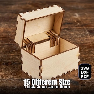 Puede incluir: Una pequeña caja de madera abierta con tapa con bisagras. La caja es de madera de color claro y tiene forma rectangular. El texto "15 Different Size Thick:3mm-4mm-6mm" está impreso en la parte inferior. La caja está sobre una superficie de madera.