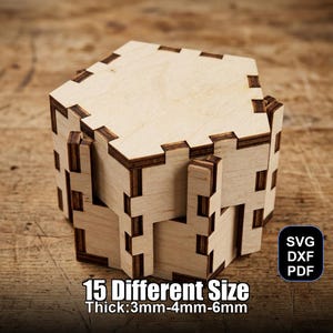 Op de afbeelding: Een lichtgekleurde houten doos met in elkaar grijpende verbindingen, met een geometrisch ontwerp. De doos is gemaakt van meerdere stukken hout, met de tekst "15 Different Size Thick: 3mm-4mm-6mm" en "SVG DXF PDF" zichtbaar.