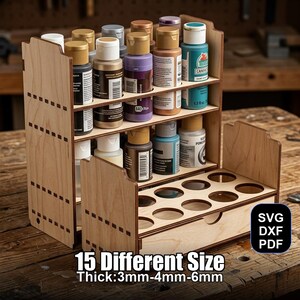 Puede incluir: Un organizador de botes de pintura de madera con múltiples estantes y un cajón. El organizador contiene varios botes de pintura de diferentes colores. El texto "15 Different Size Thick:3mm-4mm-6mm" es visible. El diseño incluye formatos de archivo SVG, DXF y PDF.