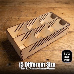Op de afbeelding: Een houten organizer met meerdere sleuven en verdelers. De doos is gemaakt van lichtgekleurd hout en heeft een reeks schuine sleuven. Tekst op de afbeelding luidt "15 Different Size Thick: 3mm-4mm-6mm" en bevat SVG-, DXF- en PDF-bestandstype-pictogrammen.