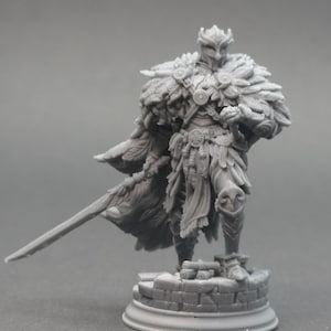 Op de afbeelding: Gedetailleerd miniatuurbeeldje van een krijger in sierlijk harnas, met een zwaard. Het figuur is versierd met gevederde accenten en ingewikkelde details, staand op een stenen voet. De kleur is een gedempt grijs.