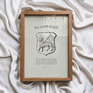 May include: A framed print with the text "The LAMB of GOD" at the top. The print features a black and white illustration of a lamb holding a flag within a shield. The frame is made of light brown wood.