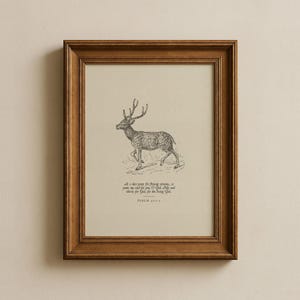 May include: A framed print featuring a detailed pen and ink drawing of a deer with large antlers. The artwork is set against a cream-colored background and includes text from Psalm 42:1-2. The frame is a warm brown color.