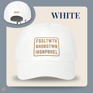 White baseball cap with the text "WHITE" and "J3:16". The front of the cap features a brown rectangular design with the text "FGSLTWTH GHOBSTWBI HSNPBHEL". The cap has an adjustable strap.